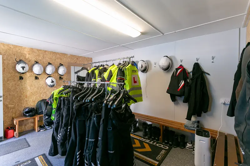 Gear room with helmets on the wall and rails of motorcycle jackets and hi-vis vests