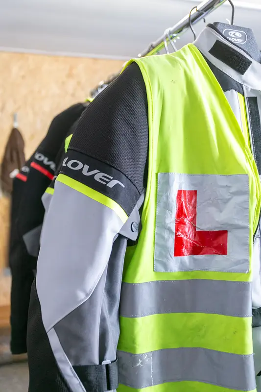 Hi-vis learner vest with a red L plate hanging over a motorcycle jacket
