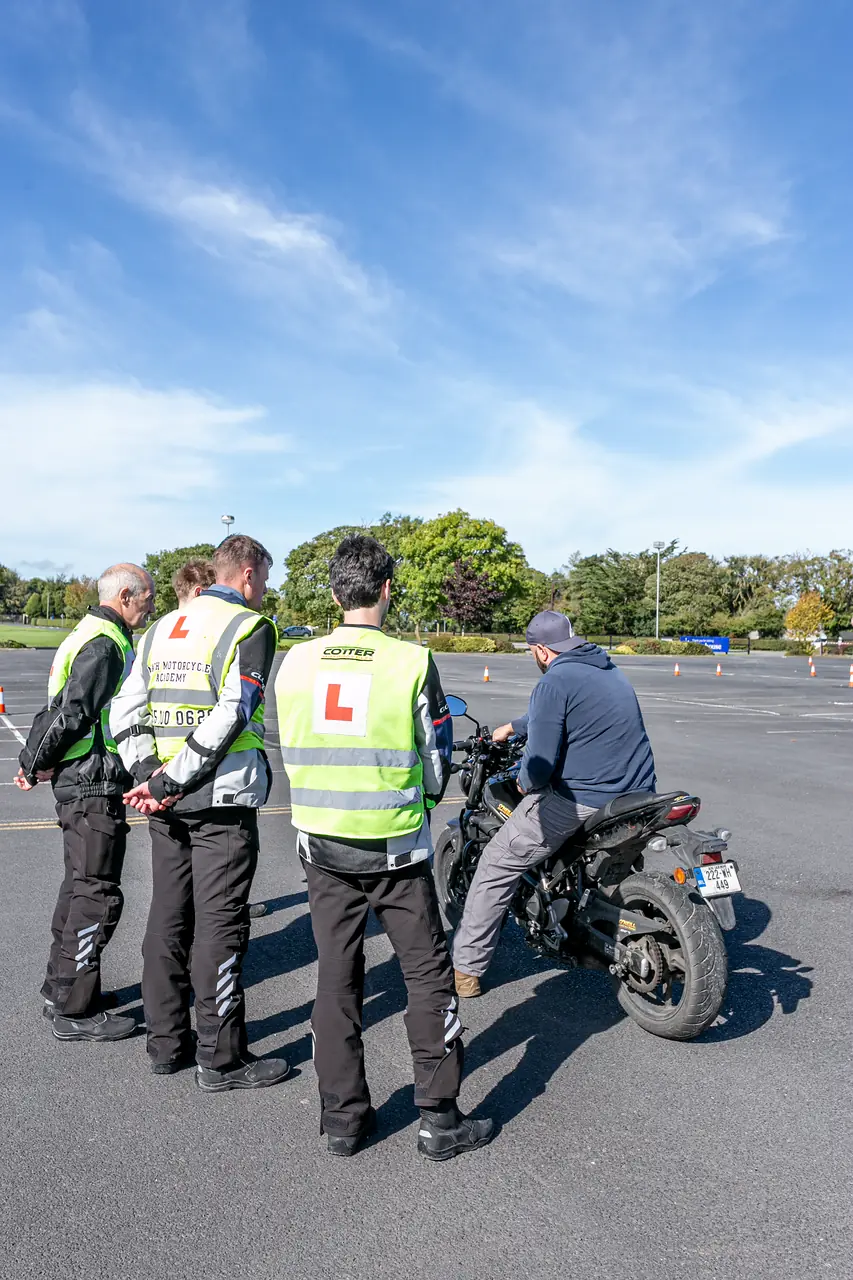 Instructor and learners in L-plate vests watching a rider on the O'Neill Motorcycle Training yard