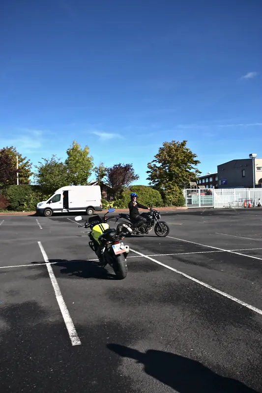 Learner rider in a hi-vis vest turning on a motorcycle between the painted lines of the yard
