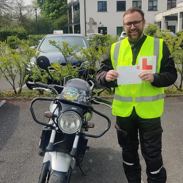 Rider in hi-vis holding their certificate beside a training motorcycle