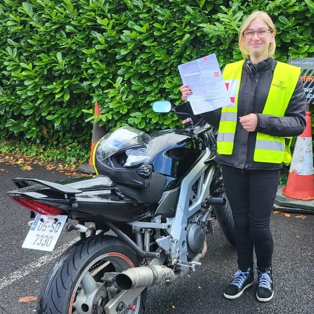 Rider holding their test pass certificate next to a Suzuki motorcycle