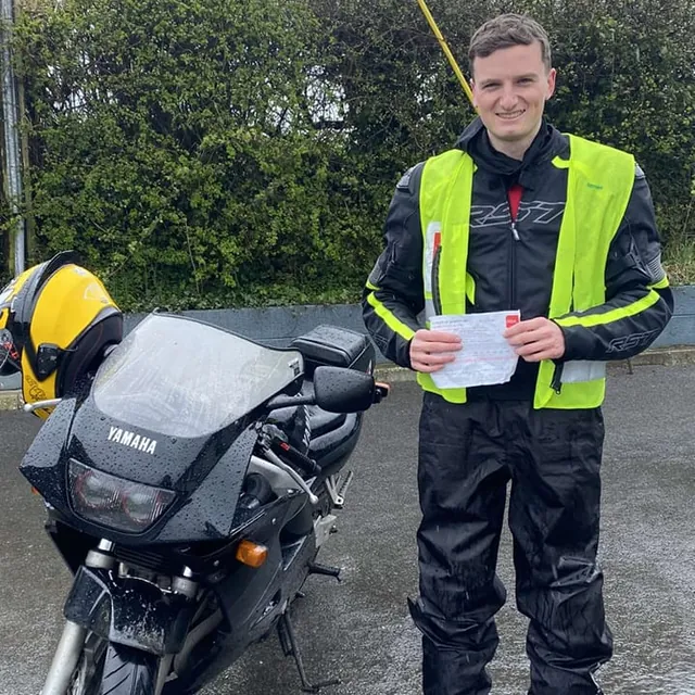 Rider with their certificate beside a Yamaha motorcycle on a wet day